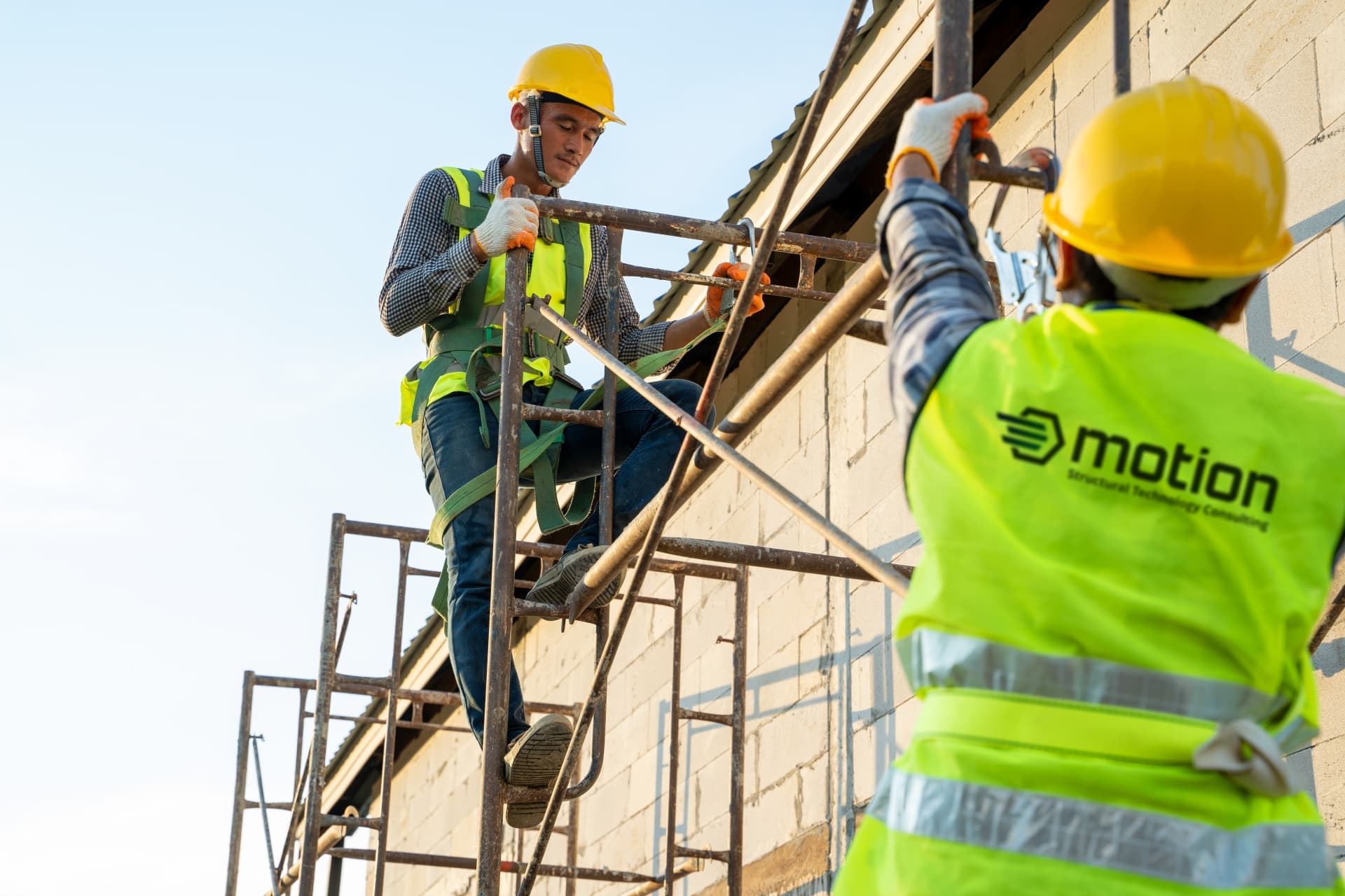 Two men in safety vests are positioned on scaffolding, engaged in construction work, highlighting workplace safety measures.