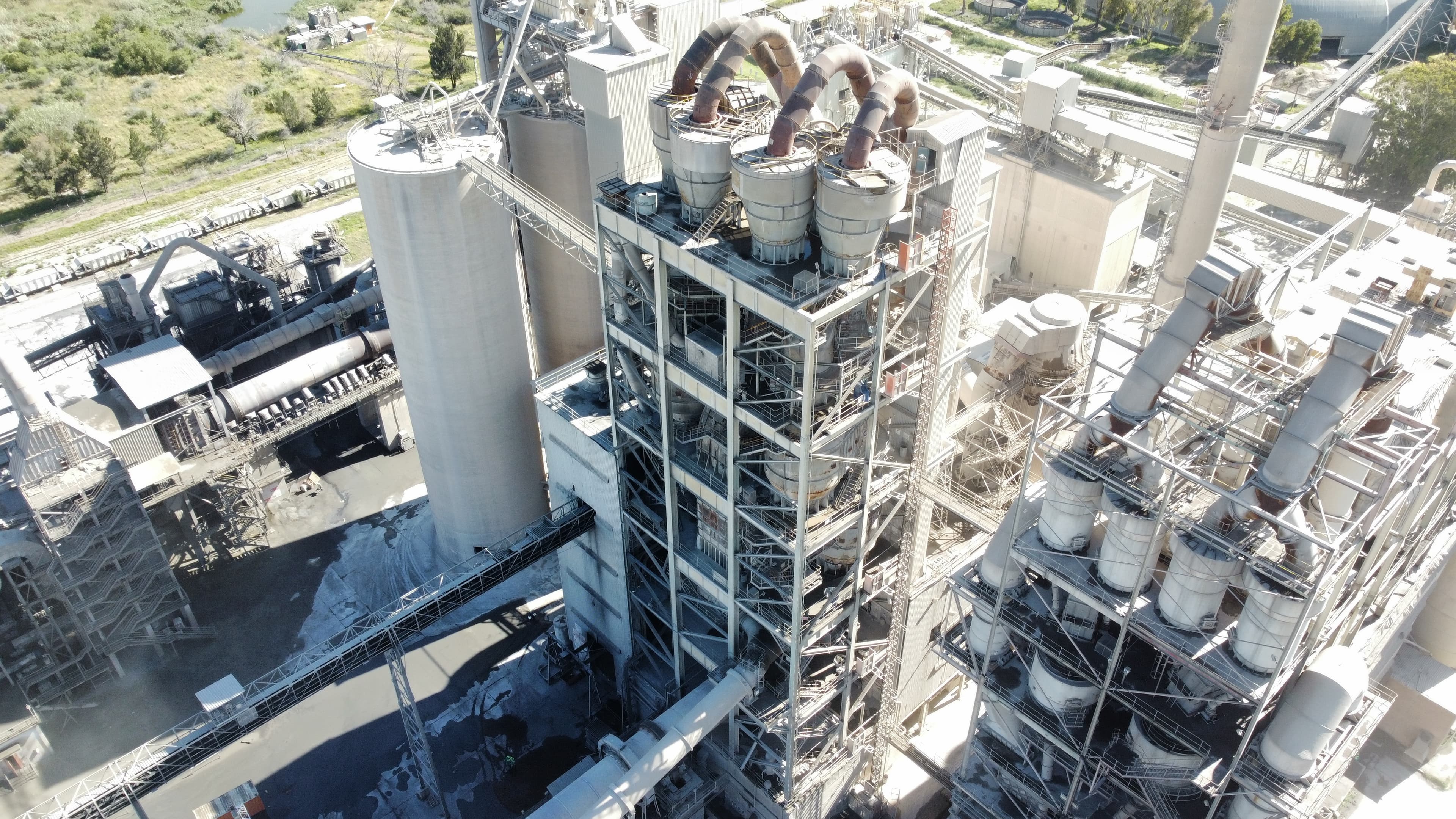 Aerial view of a cement plant showcasing large silos, machinery, and surrounding industrial landscape.